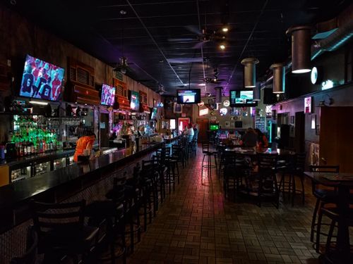 Free A dimly lit modern bar interior featuring a long counter and multiple screens, creating a cozy urban atmosphere. Stock Photo