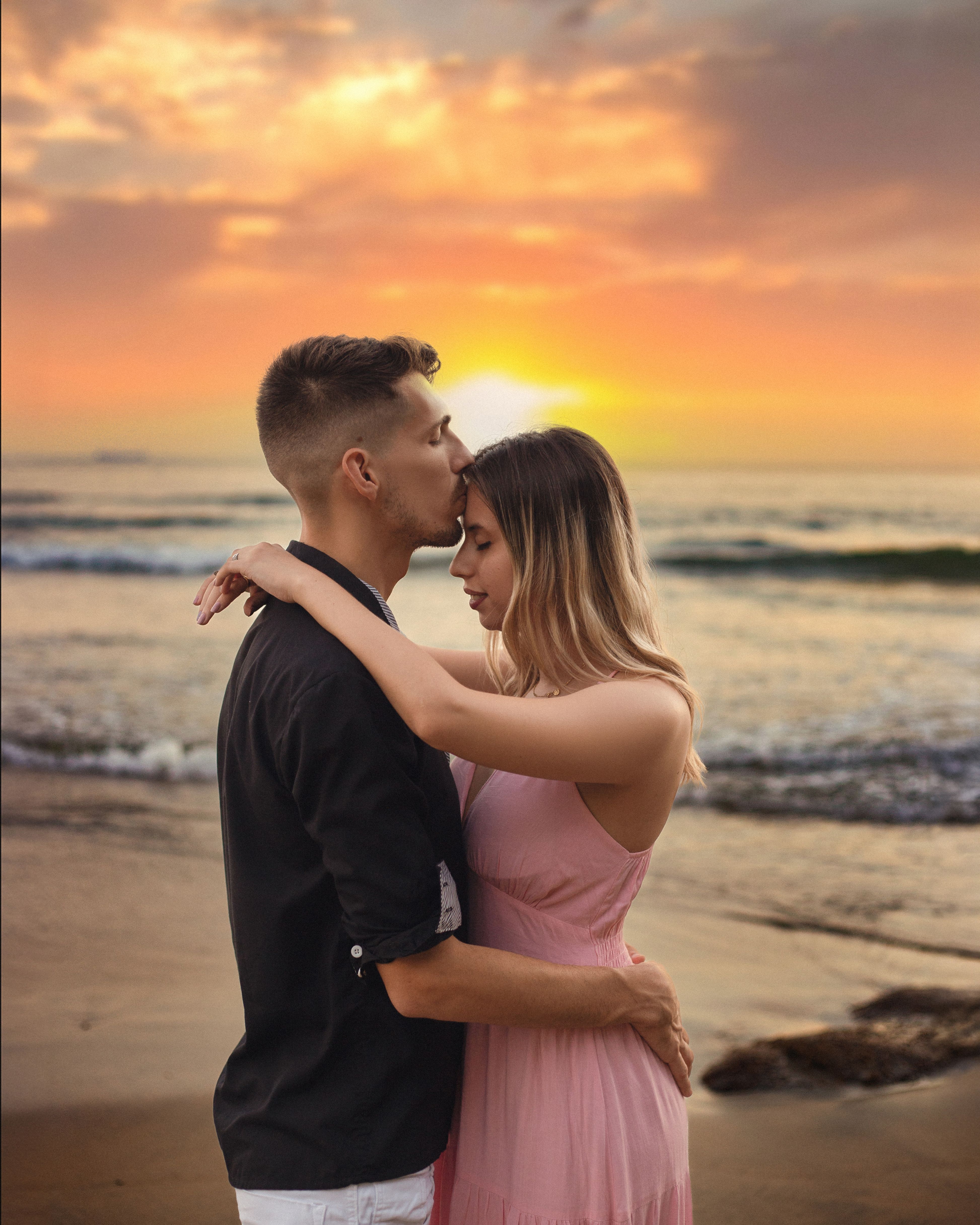 Couple embraces on the beach during a stunning sunset, showcasing love and tranquility.
