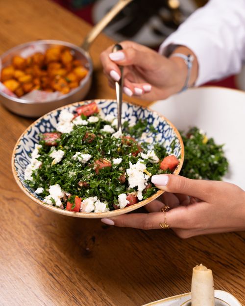 Free Hands serving tabbouleh salad with parsley, tomatoes, and feta cheese in a blue-patterned bowl. Stock Photo