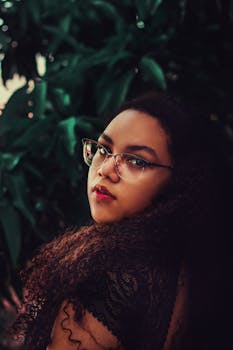一位卷发戴眼镜的女子，在绿植前摆出令人惊叹的肖像姿态