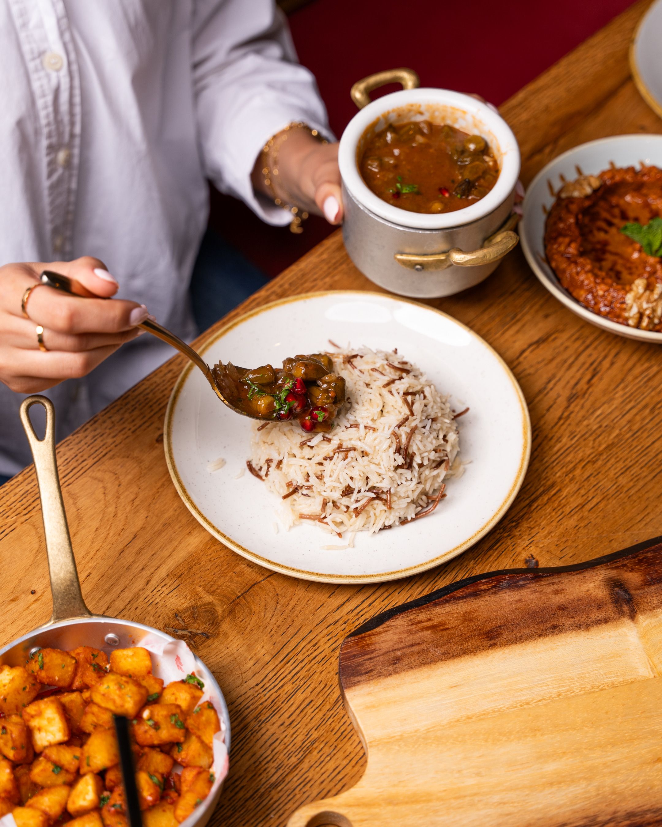 Close-up of a diverse meal setting with rice, curry, and potatoes served on a wooden table.