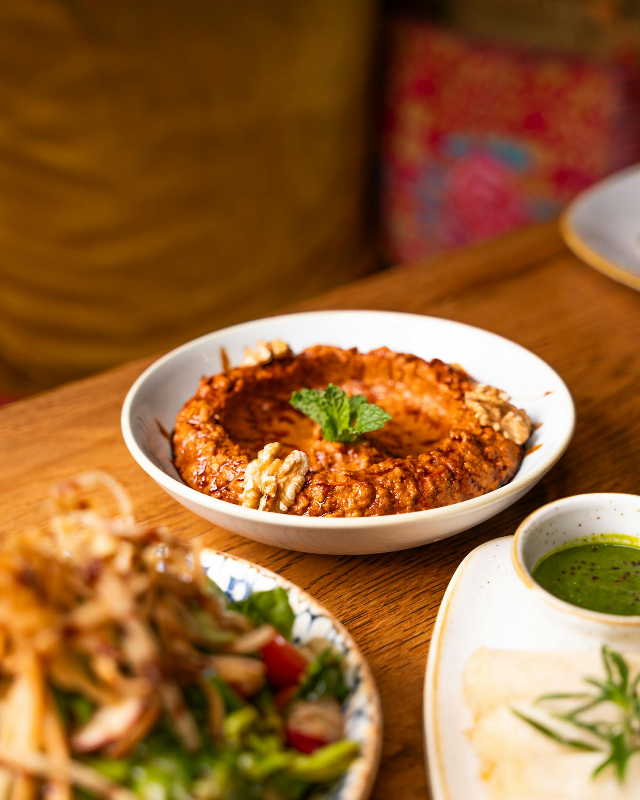 Bowl of chunky muhammara dip garnished with walnuts and Aleppo pepper flakes, served with torn pita bread