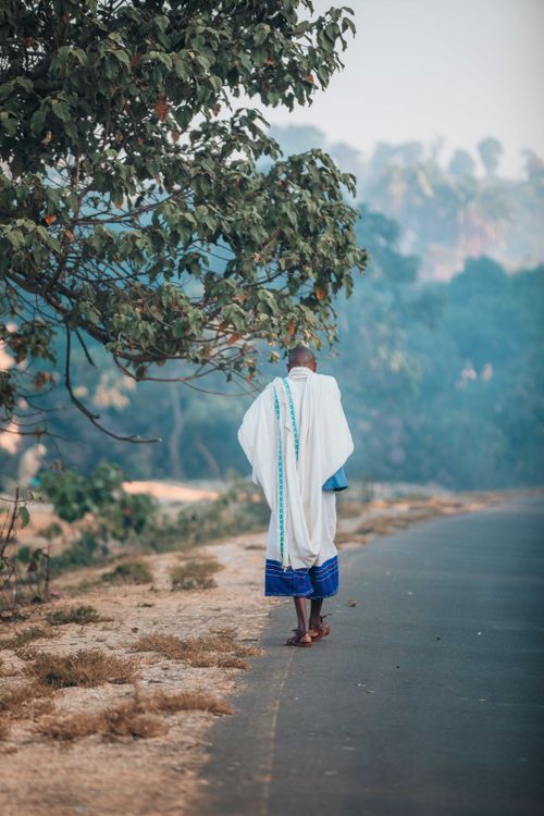Free A man in traditional clothing walks down a rural road surrounded by nature. Stock Photo