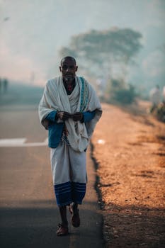 African man in traditional attire walking on a road during sunrise, capturing cultural essence.