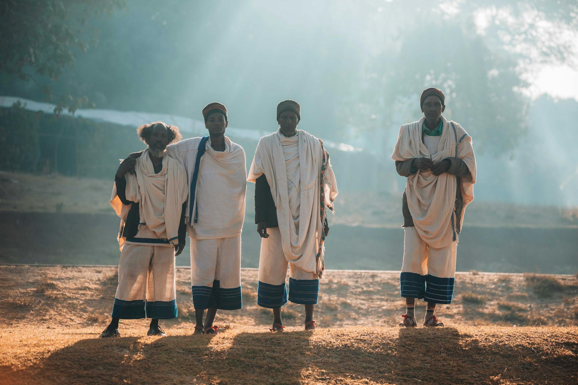 A group of Ethiopian men in traditional attire, standing in a rural landscape at sunrise.