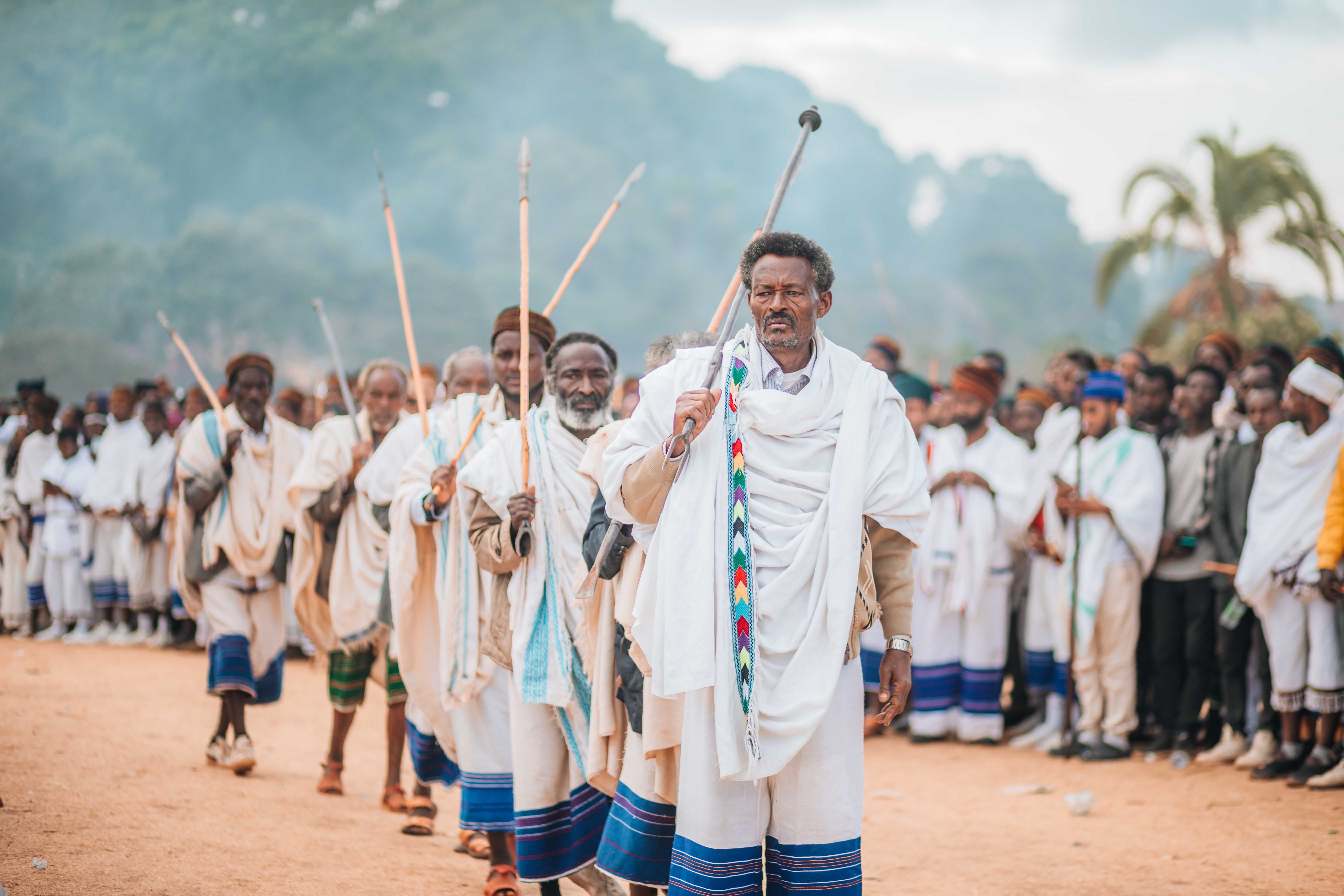 A group of African men in traditional robes participate in a cultural ceremony outdoors.