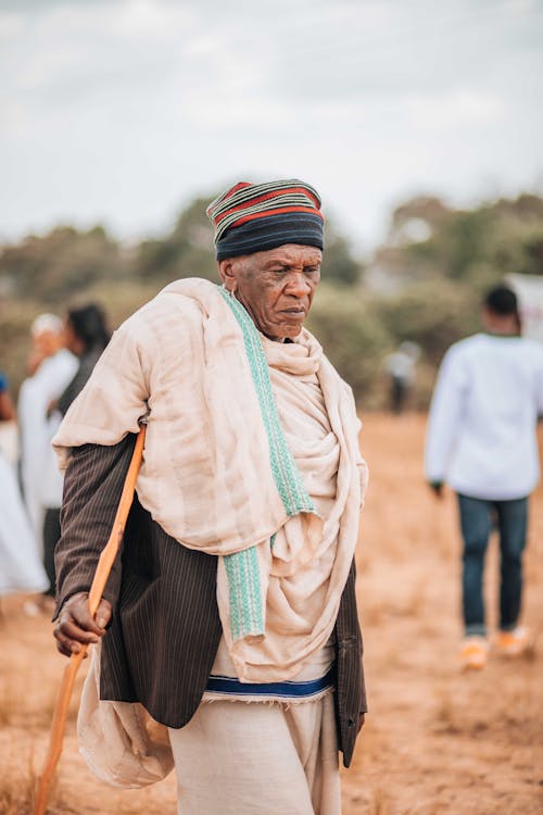 An old man with a cane walking through a field