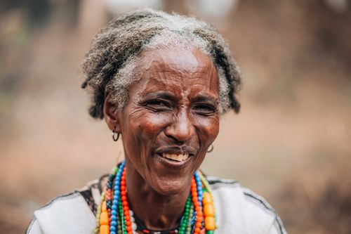 Free Elderly woman smiling warmly, wearing vibrant beaded necklaces outdoors. Stock Photo