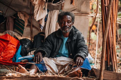 Free Elderly man sitting in a makeshift shelter, displaying rural village life. Stock Photo
