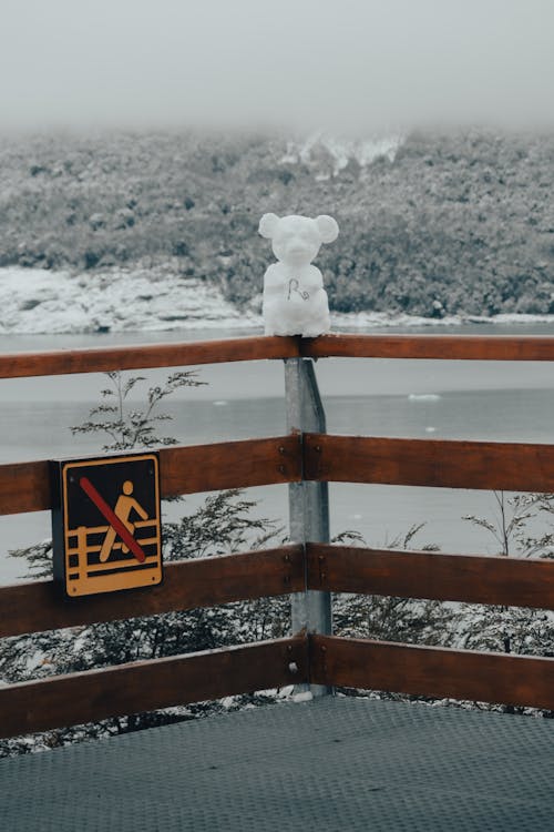 A teddy bear sitting on a railing next to a sign