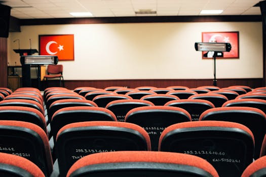 An empty conference room featuring red seats, a stage, and Turkish flags, ready for a meeting or presentation.
