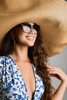Elegant woman posing in a floral summer dress with a large straw hat and sunglasses.