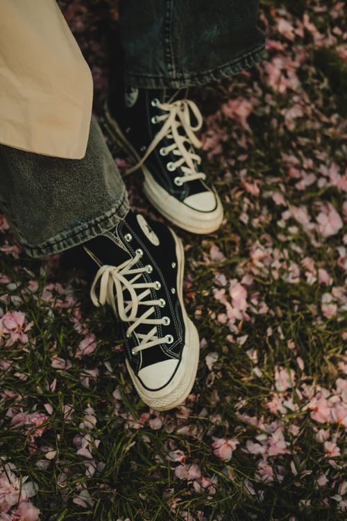 Free Close-up of black sneakers on grass with scattered pink flowers, evoking a laid-back vibe. Stock Photo