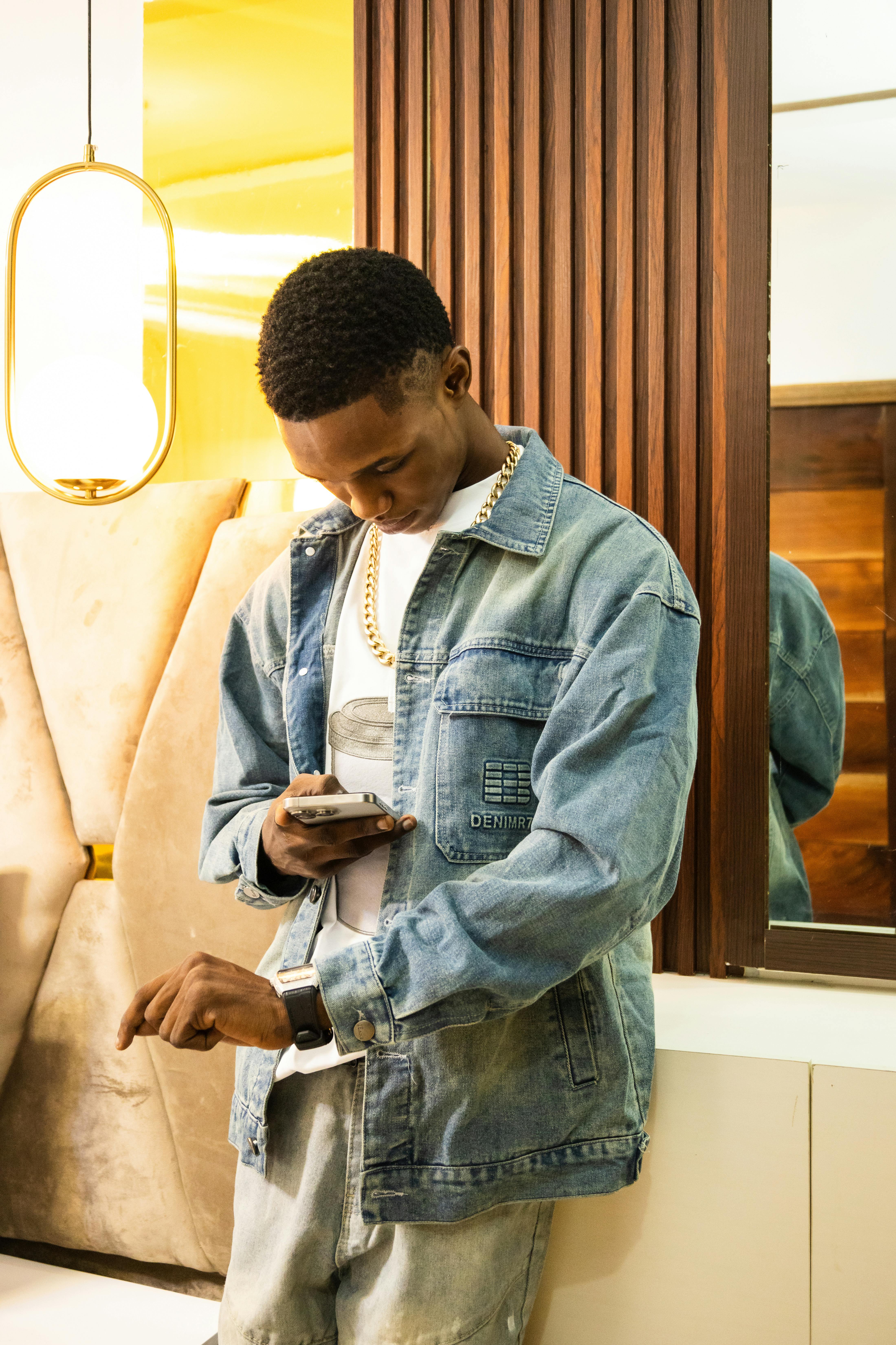 Trendy young man wearing denim jacket and checking his phone indoors.