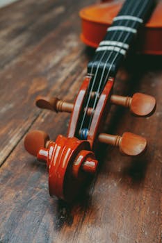 Detailed view of a violin neck and scroll on a rustic wooden table, showcasing craftsmanship and texture.