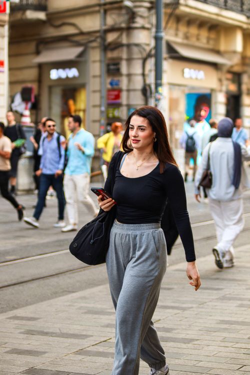 Free Young woman in casual attire walks confidently through a busy city street, phone in hand. Stock Photo