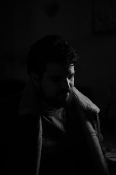 A dramatic black and white portrait of a man with a beard in a cozy jacket.
