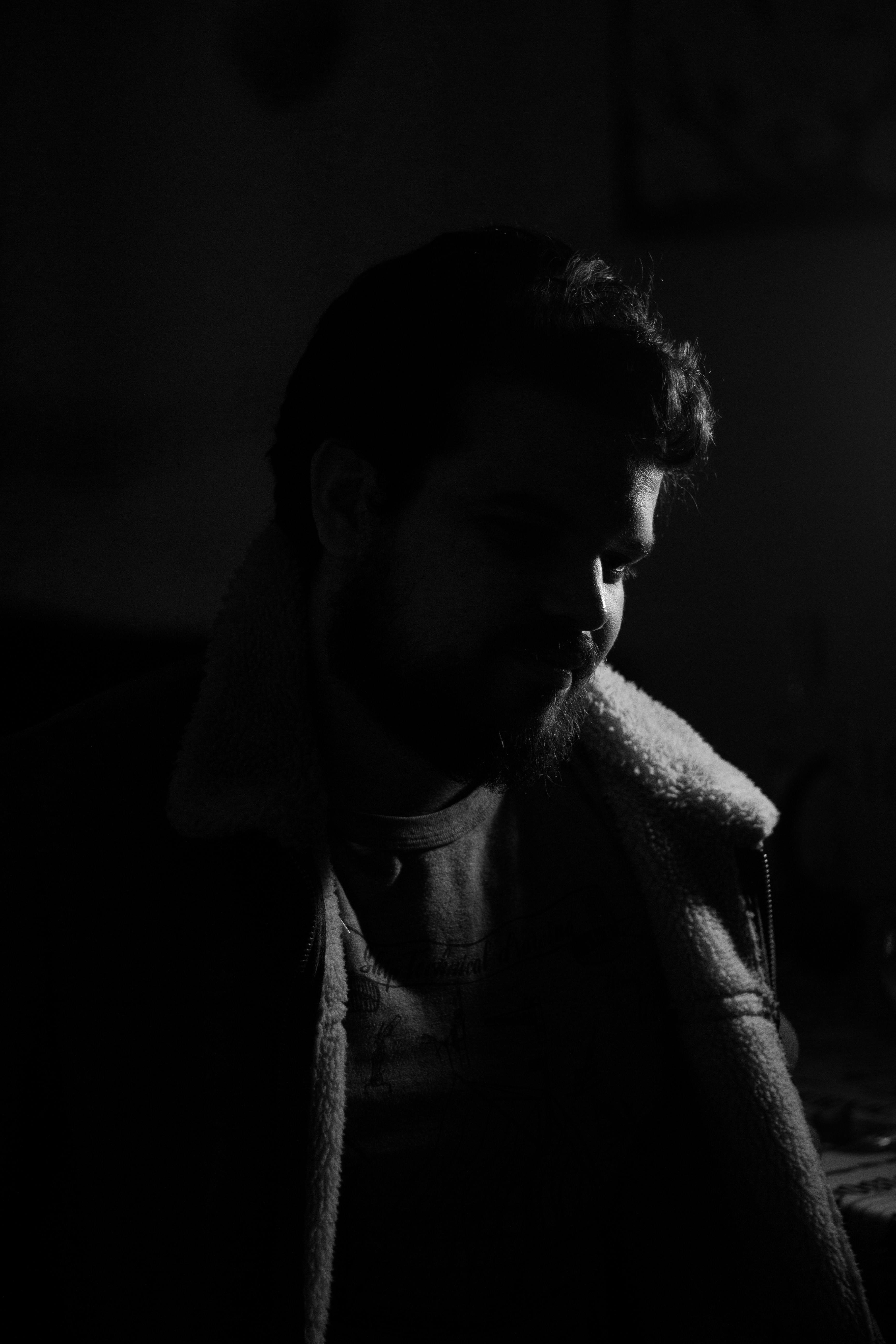 Profile of a bearded man wearing a shearling jacket in a dark setting.
