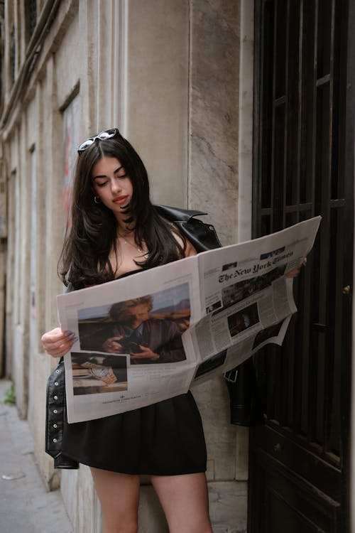 A woman in a black dress is reading a newspaper
