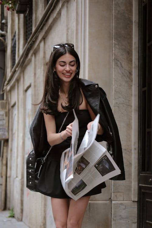 A woman in a black dress and jacket is reading a newspaper