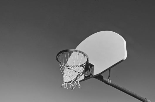 Black and white photo of an outdoor basketball hoop set against a clear sky, emphasizing sports equipment.