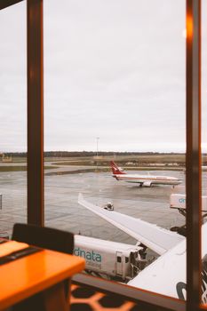 Airplanes parked at Melbourne Airport terminal, viewed from a glass window on a cloudy day.