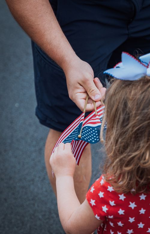 Free Close-up of child receiving a small American flag during a patriotic event outdoors. Stock Photo