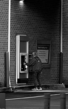 Black and white photo of a man using an ATM in the urban setting.