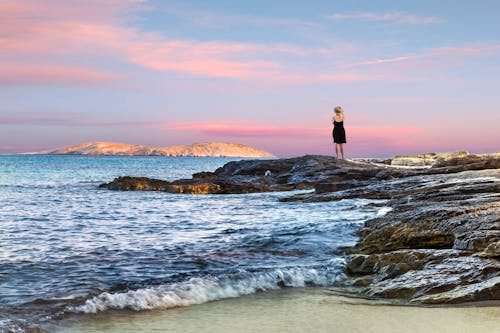 Woman Standing on Rocky Shore during Day