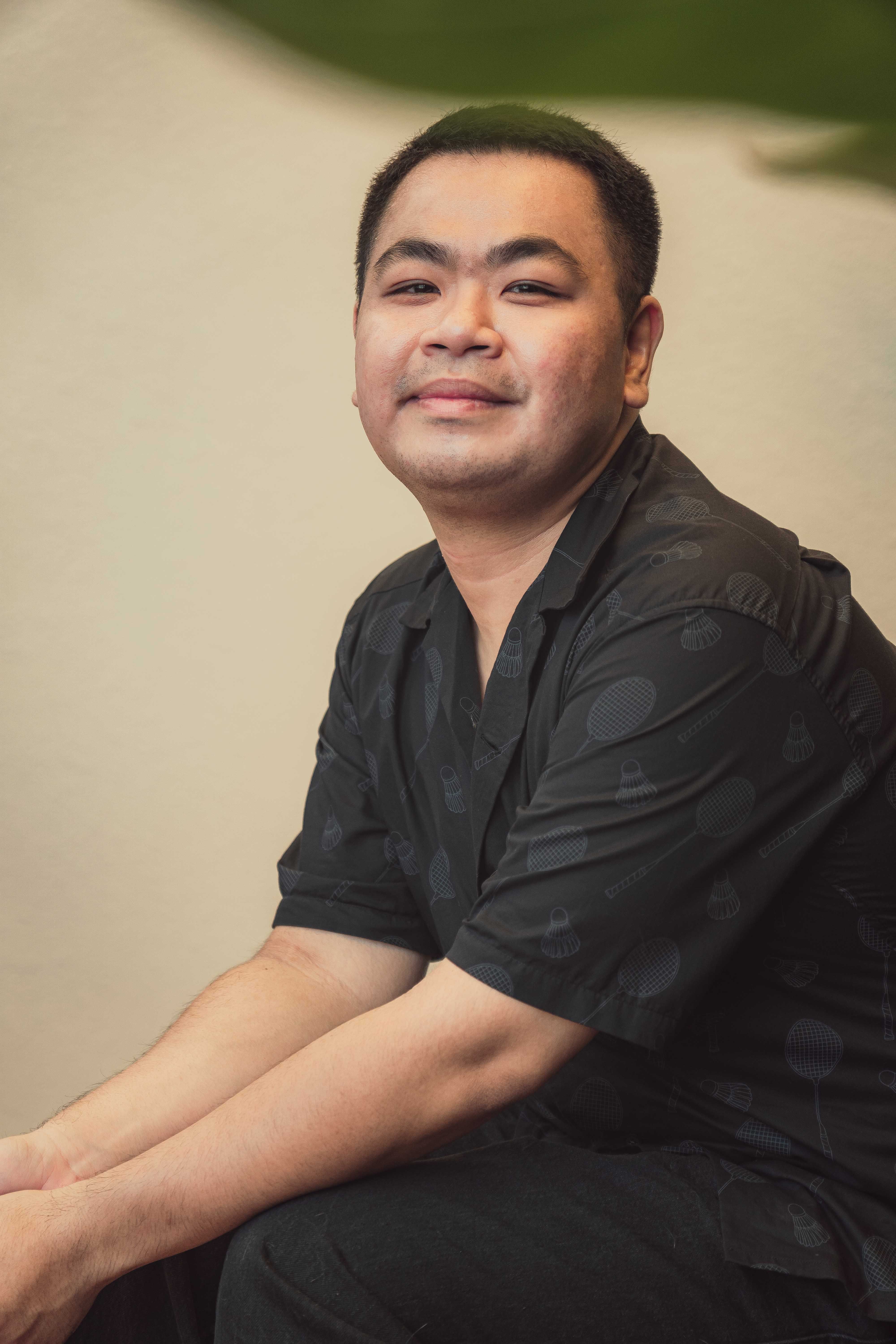 A relaxed portrait of a man sitting indoors in warm lighting, exuding a calm demeanor.