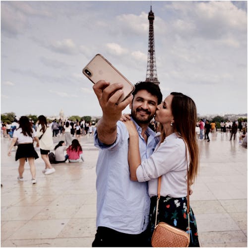 Photo of Hugging Couple Taking Selfie With a Crowd of People and The Eiffel Tower in the Background