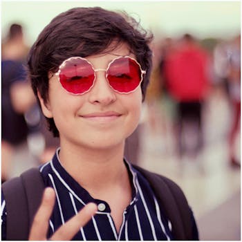 Smiling teenager in Paris wearing unique red sunglasses and a striped shirt, showing a peace sign.