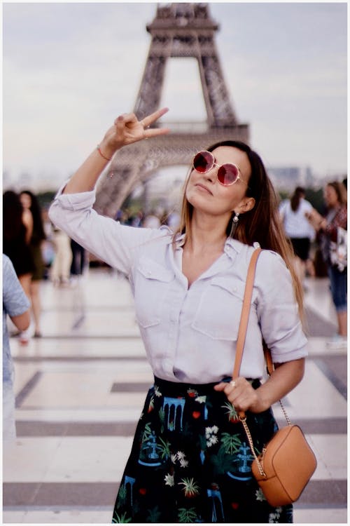Photo of a Woman in White Long-sleeved Shirt Standing Near Eiffel Tower