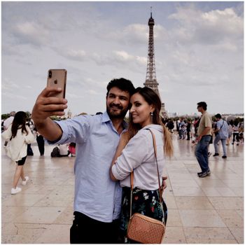 A couple taking a selfie near Eiffel Tower in Paris, capturing a romantic moment.