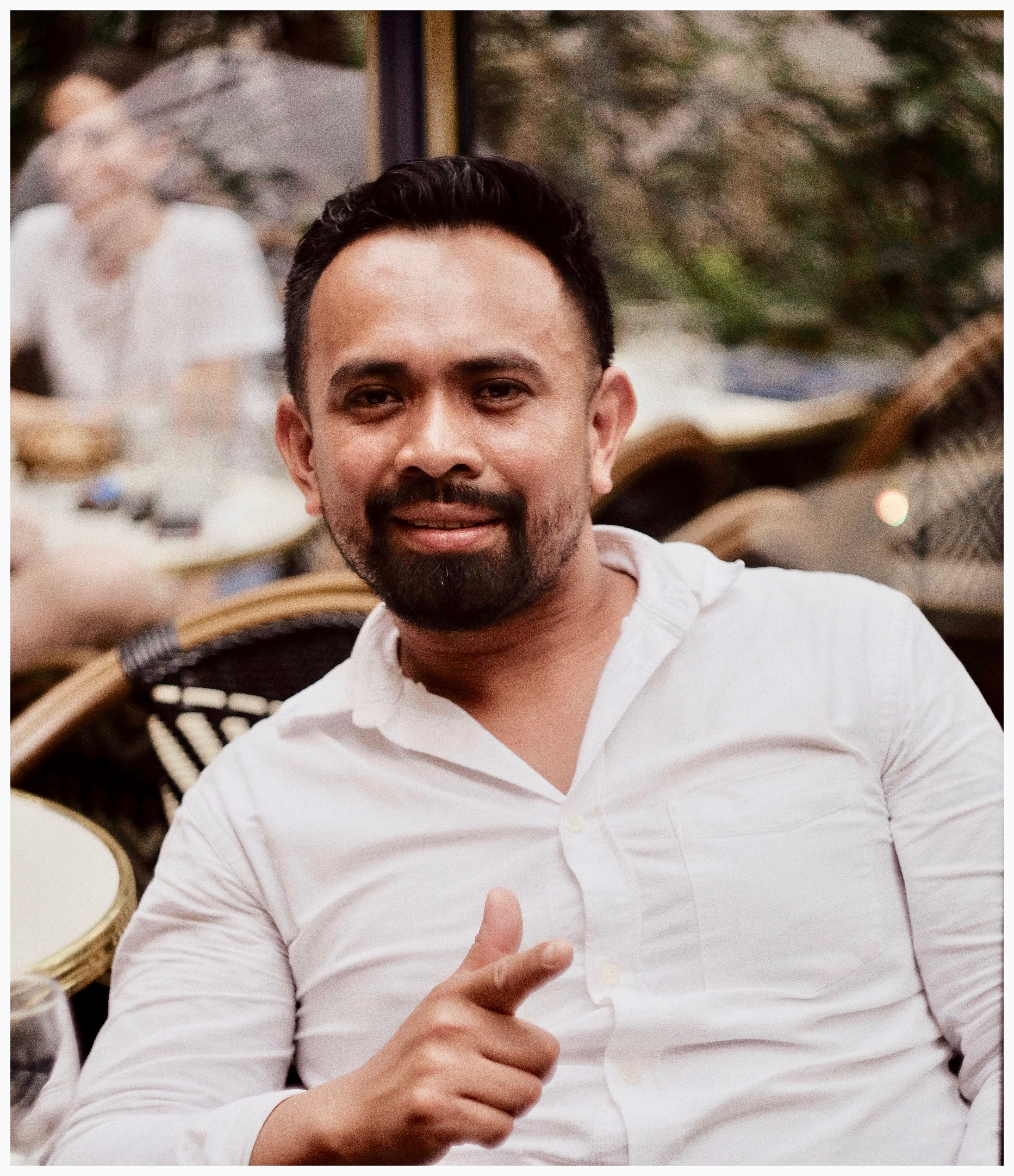 Portrait of a smiling man relaxing at a Paris café in a white shirt, enjoying the atmosphere.