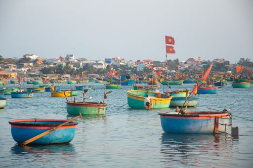 Free Colorful traditional fishing boats in a Vietnamese harbor with calm water and clear sky. Stock Photo