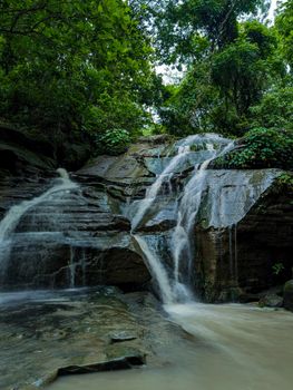 A tranquil waterfall cascades over rocks in a verdant forest, creating a serene nature scene.