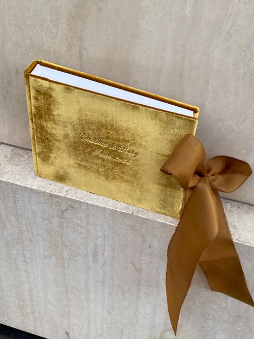 Free Gold velvet book with a brown silk bow on a marble surface, offering a luxurious gift presentation. Stock Photo