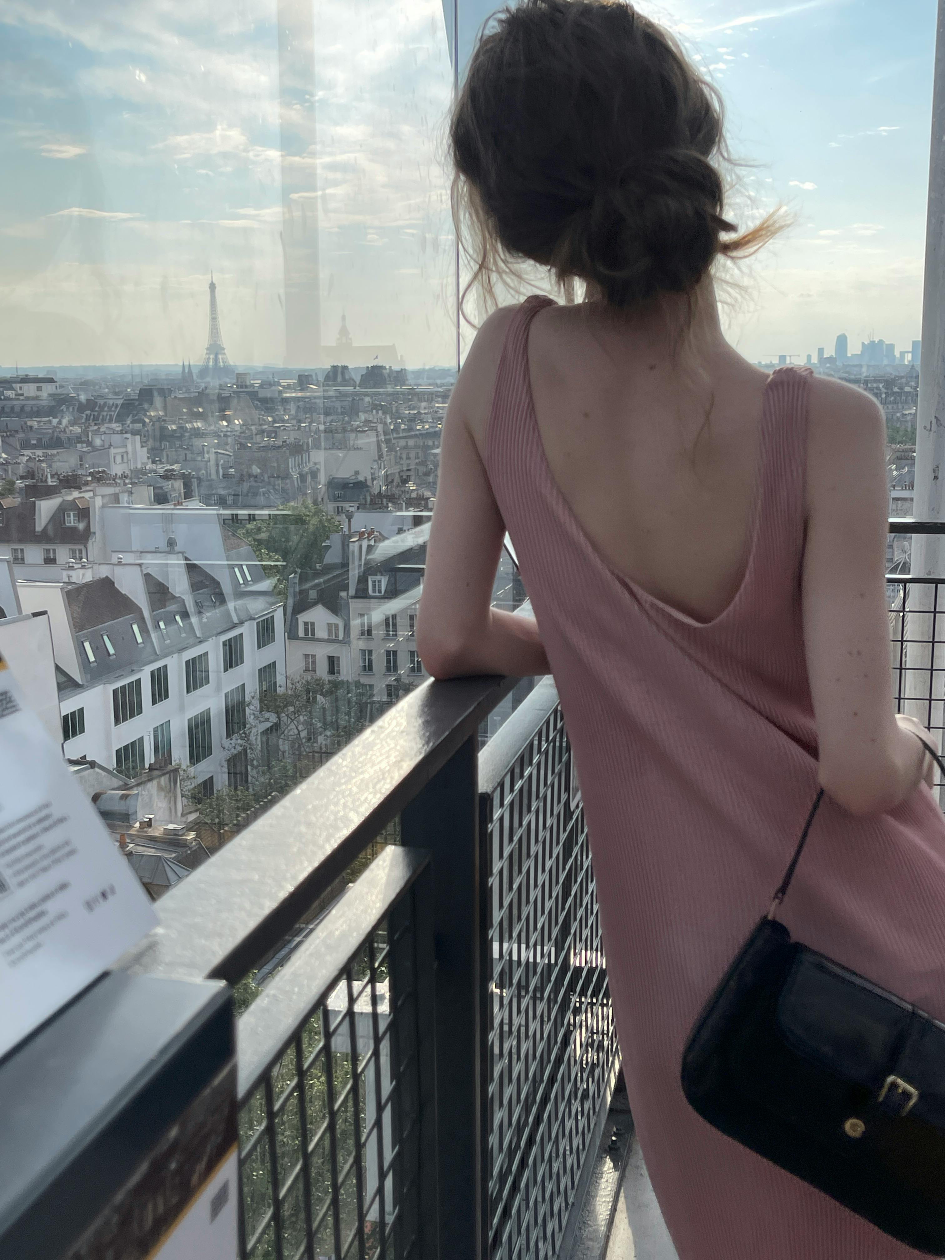 A woman in a pink dress overlooks the Paris skyline with the Eiffel Tower in view.