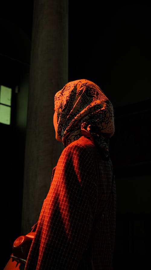 A woman in a red coat and scarf is standing in a dark room