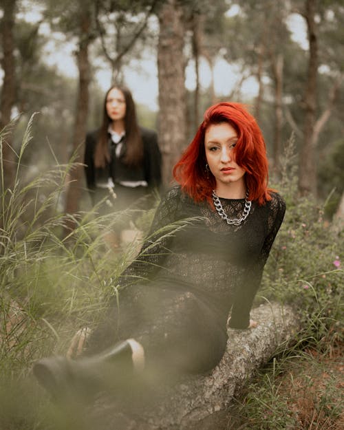 Two women with red hair sitting on a log in the woods
