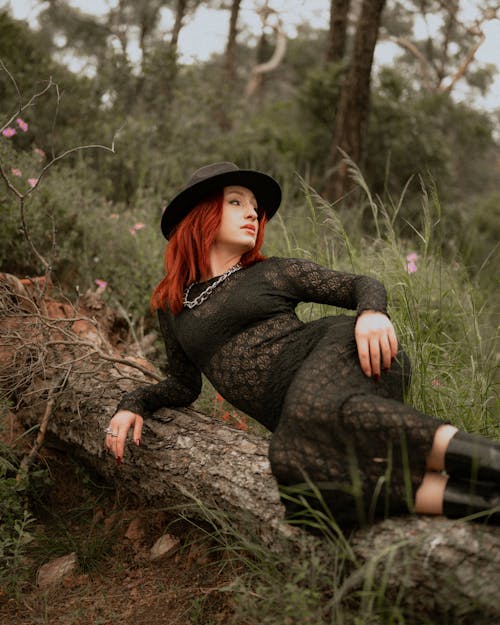 A woman in a hat and dress sitting on a log