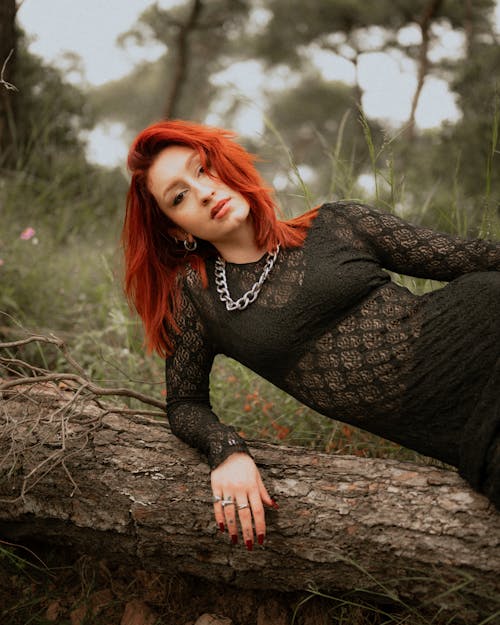 A woman with red hair and black dress laying on a tree