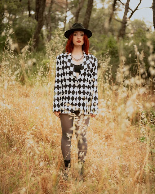 A woman in a black and white checkered jacket and hat standing in a field