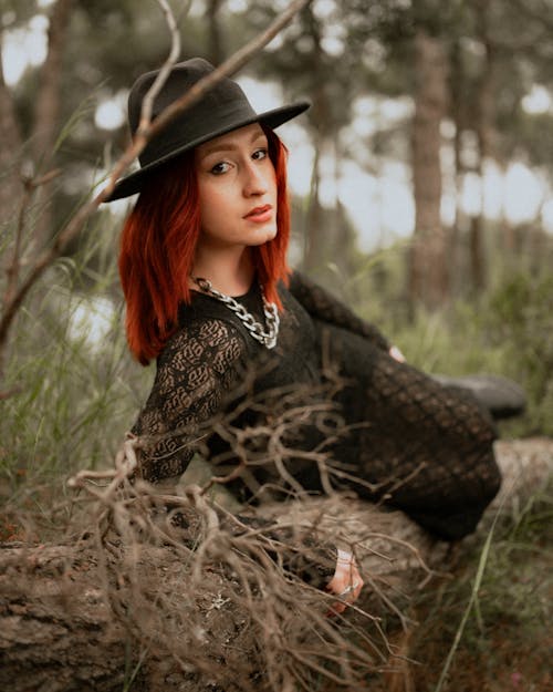 A woman with red hair and a hat sitting on a tree
