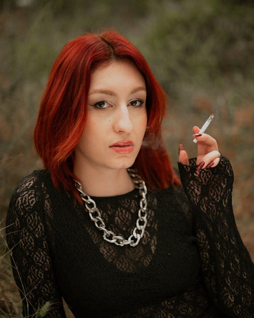 A woman with red hair and a black dress smoking a cigarette