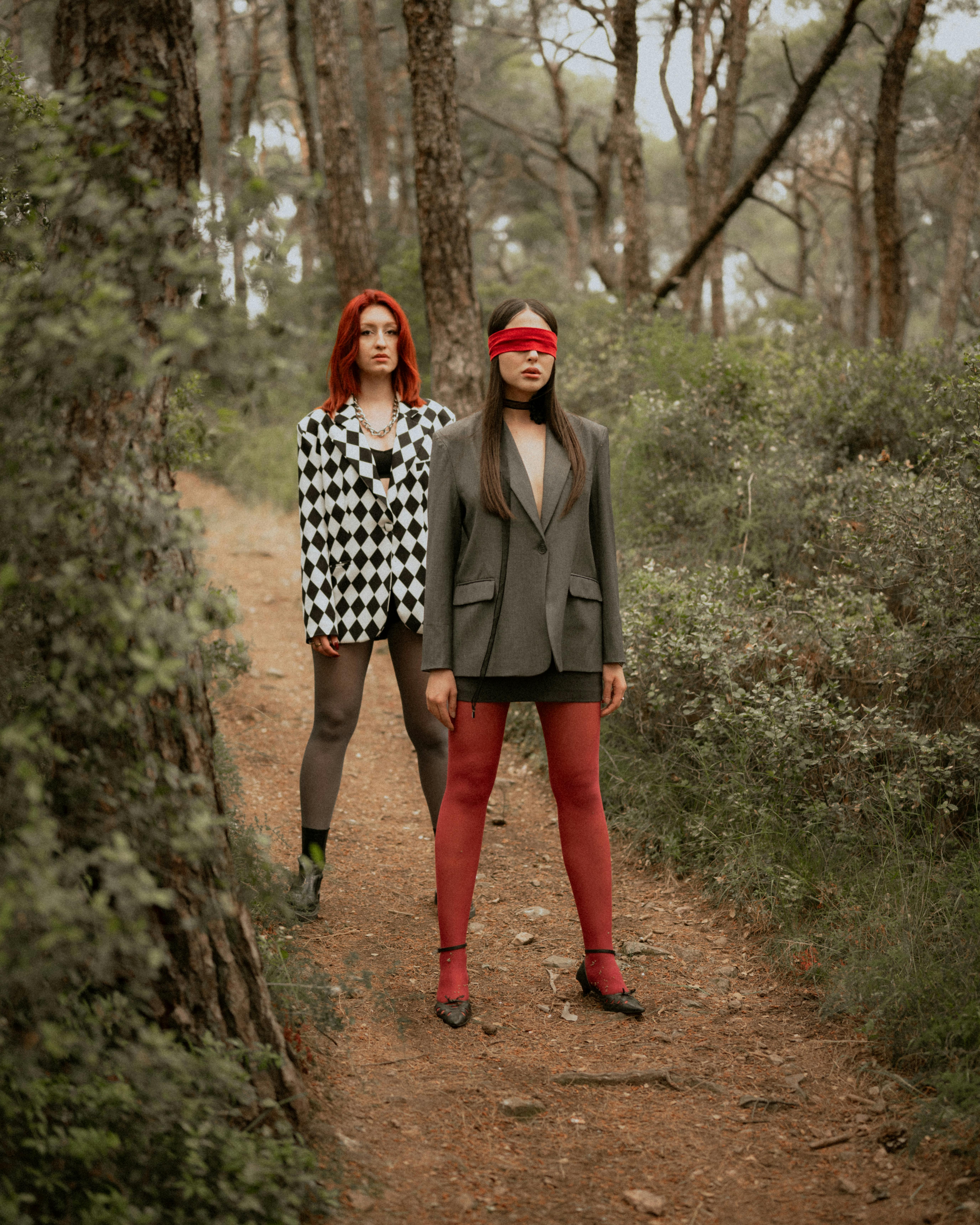 redhead standing behind woman wearing red blindfold in forest