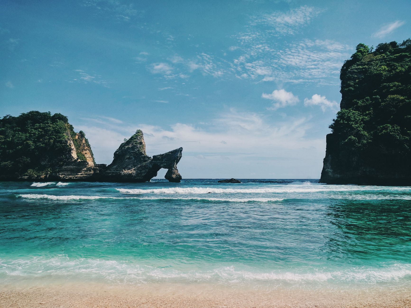 Scenic view of Bali's coastline with unique rock formations, clear turquoise waters, and a serene sky.