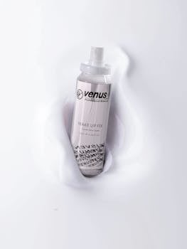 A sleek makeup fix spray bottle by Venus rests on a smooth white surface.