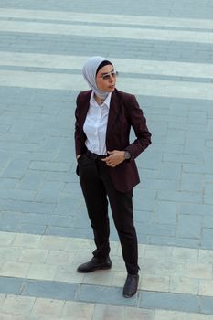 Stylish woman in hijab and formal attire posing confidently outdoors.